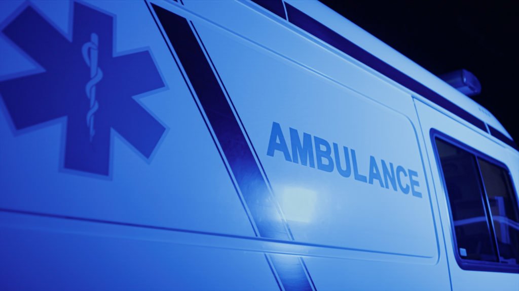 Closeup emergency body of car with logo. Detailed view of ambulance vehicle with emblem. Medical symbols on first aid van. Red and blue lights flashing on car at night on street. First aid concept